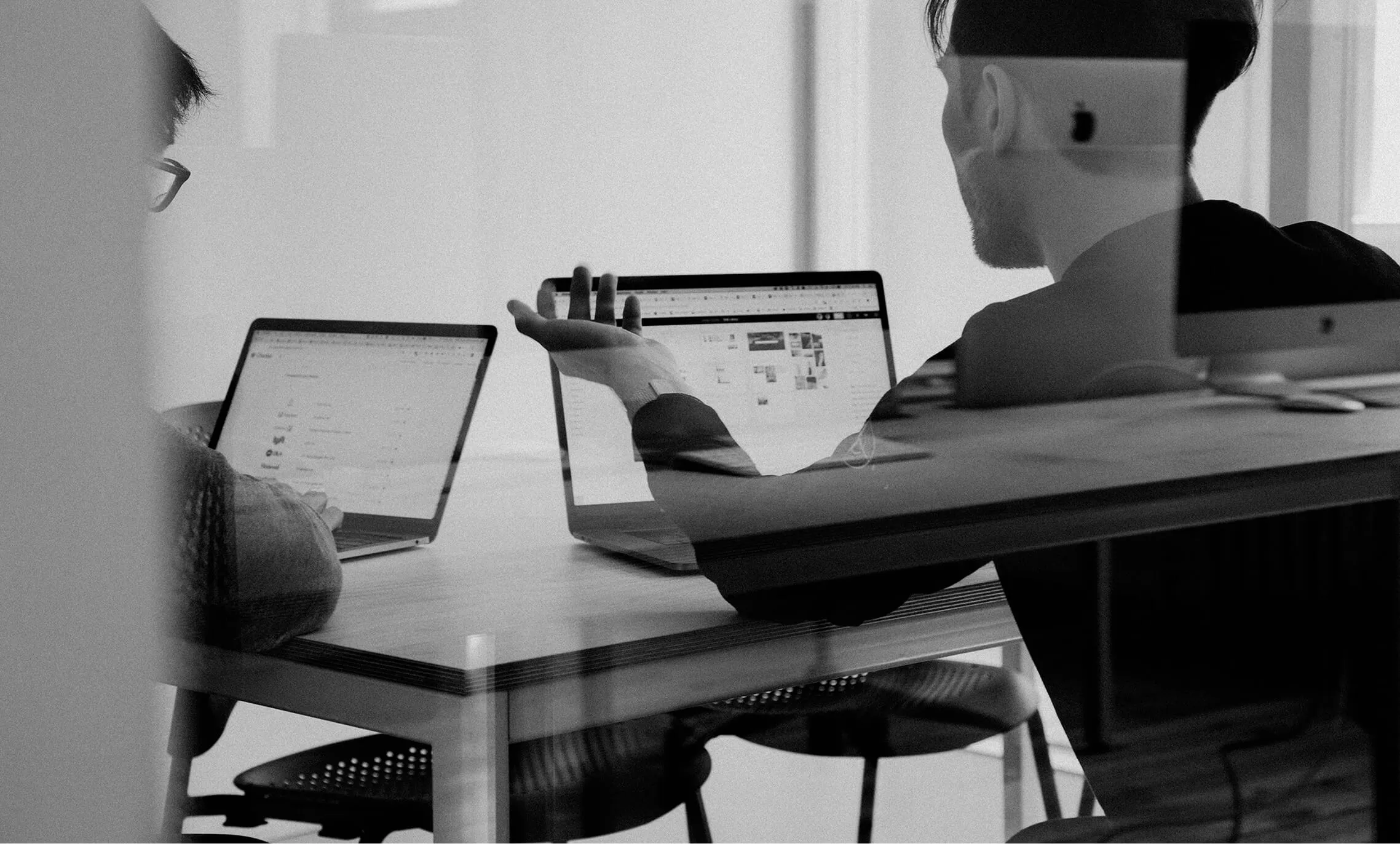 Black and white photo of people working at a table with laptops, discussing a website on screen.
